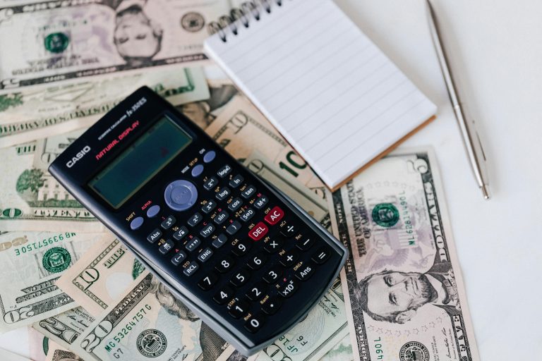 Calculator and notepad placed on USA dollars stack. Concepts of insurance, finance, economics, payment, worker's compensation