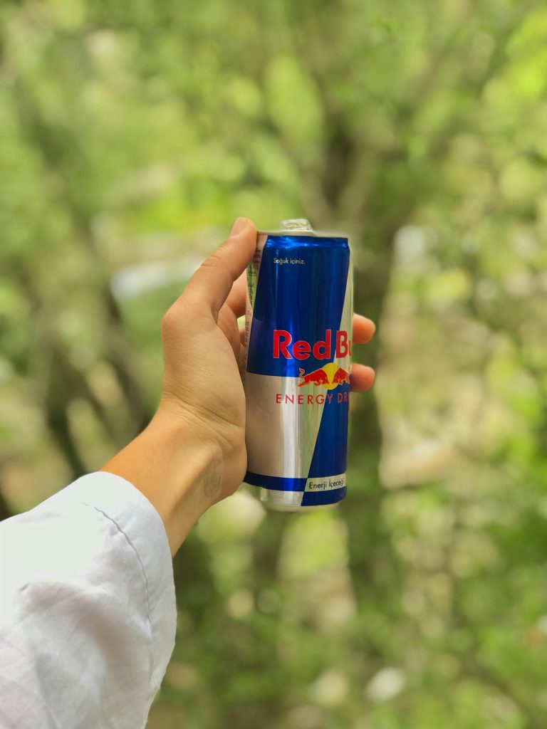 A hand holding a Red Bull energy drink can outdoors, highlighting the potential health risks associated with high-caffeine beverages and their impact on insurance costs.