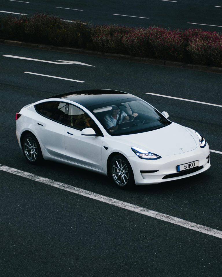 A sleek white electric vehicle (EV) cruising on a highway, highlighting the rising trend of EV adoption and the associated higher insurance premiums. This image is ideal for discussing topics like EV insurance costs, why insuring electric vehicles is more expensive than gas-powered cars, and factors influencing auto insurance rates, such as repair costs, vehicle price, and specialized maintenance requirements. Perfect for content targeting auto insurance and EV ownership considerations.