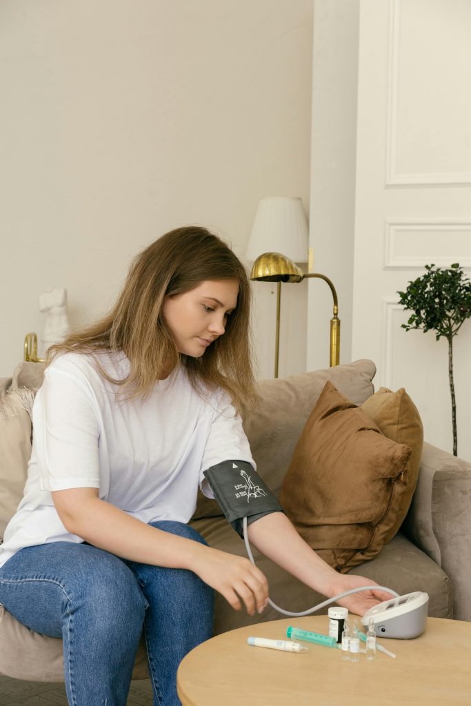 A woman checks her blood pressure at home with a digital monitor, surrounded by medical supplies, including syringes and medications. The image highlights the importance of health monitoring, which aligns with research showing that workplace health initiatives like paid sick leave can reduce injuries and improve safety, especially in high-risk industries.