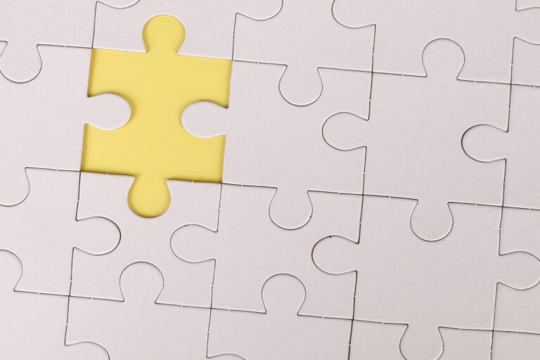 A white jigsaw puzzle with a single missing piece revealing a yellow background underneath. This image symbolizes potential gaps in insurance policy coverage, highlighting the importance of reviewing and addressing these gaps to ensure comprehensive protection for your assets, valuables, and liabilities.